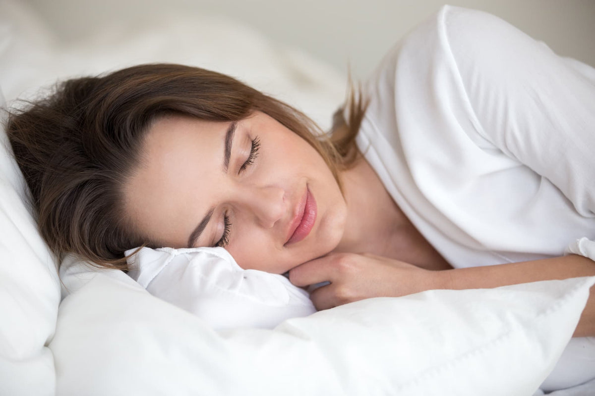 Donna che dorme serenamente a letto: il riposo come primo gesto di skincare