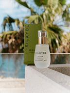 Siero Hydra-Lift accanto alla confezione verde Silkybe, con palme e piscina sullo sfondo