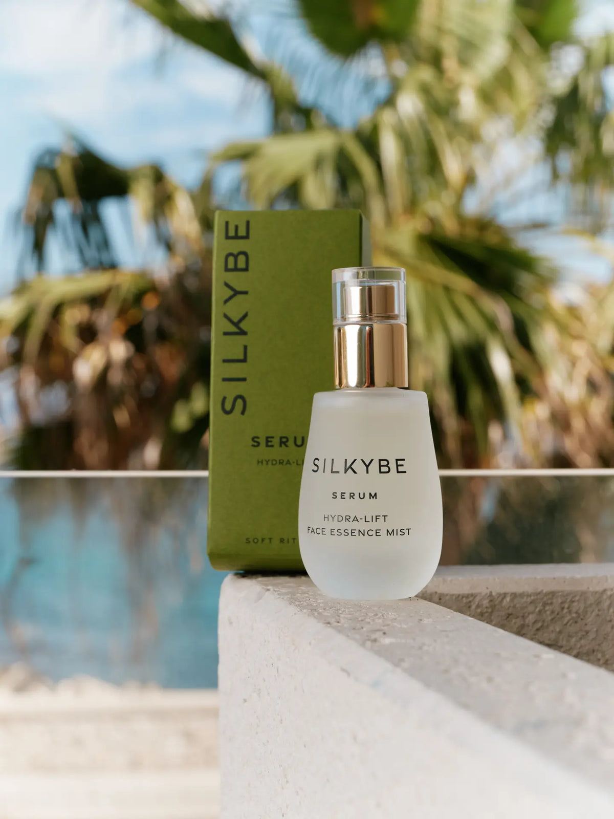Siero Hydra-Lift accanto alla confezione verde Silkybe, con palme e piscina sullo sfondo