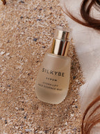 Siero Hydra-Lift posato sulla sabbia con capelli e tessuto naturale