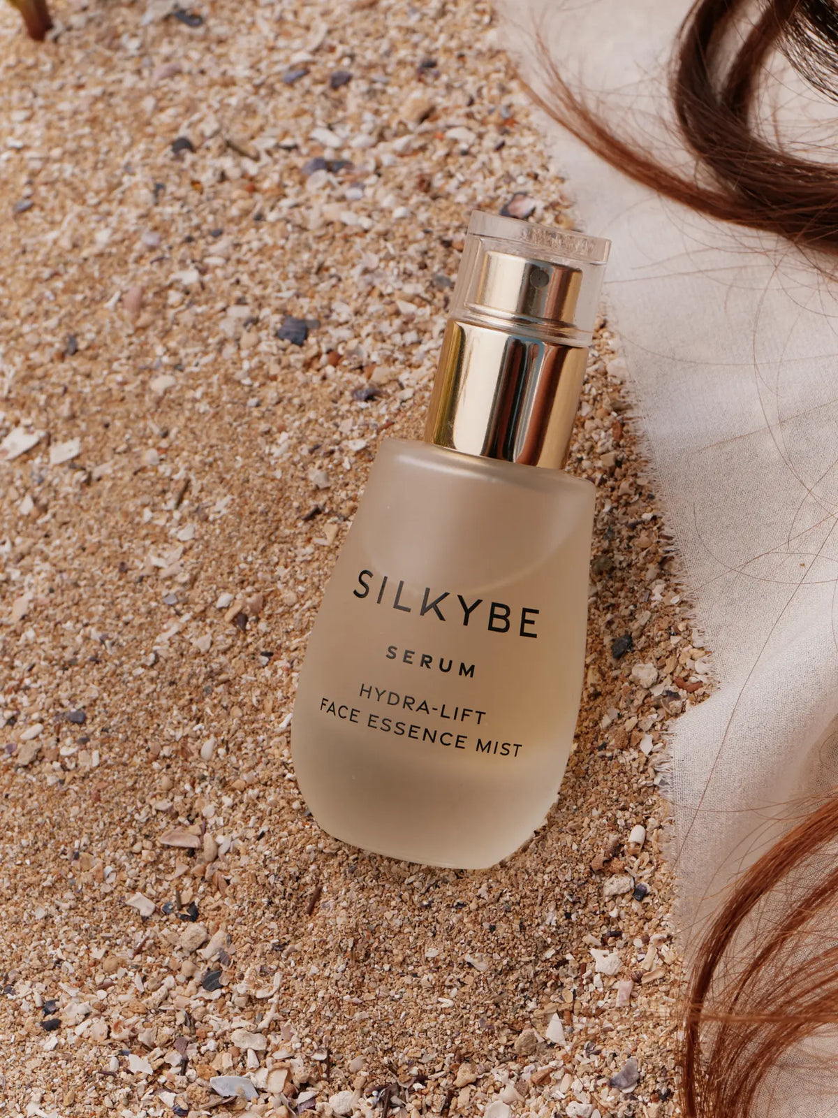 Siero Hydra-Lift posato sulla sabbia con capelli e tessuto naturale